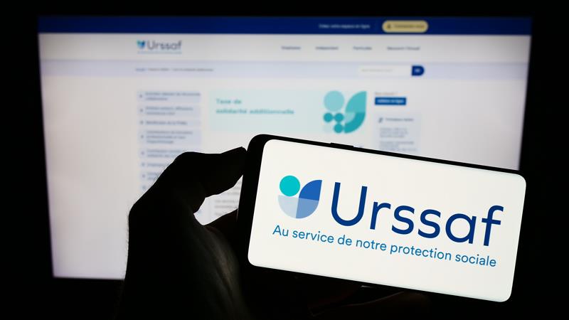 Personne tenant un téléphone avec le logo de l'Urssaf devant le portail pour le service CESU