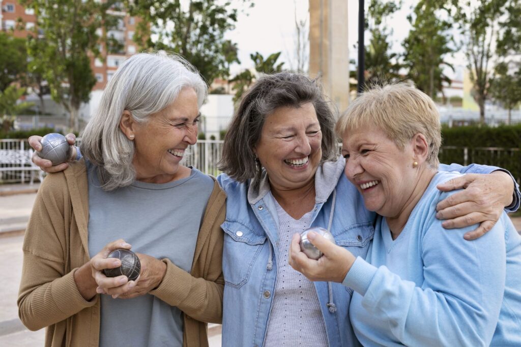 Trois femmes seniors qui jouent à la pétanque et sont joyeuses.